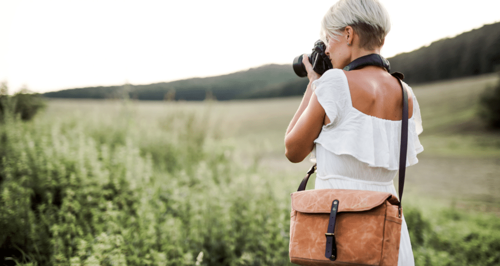 Woman taking photos of Instagrammable spots in a field surrounded by mountains